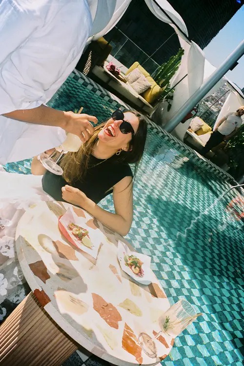 woman smiling as she's being served at her table next to the rooftop pool at the Hoxton Poblenou in Barcelona.