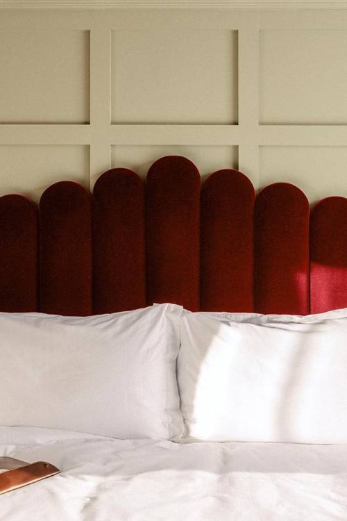 Large red velvet headboard with bedside table and art on the wall.