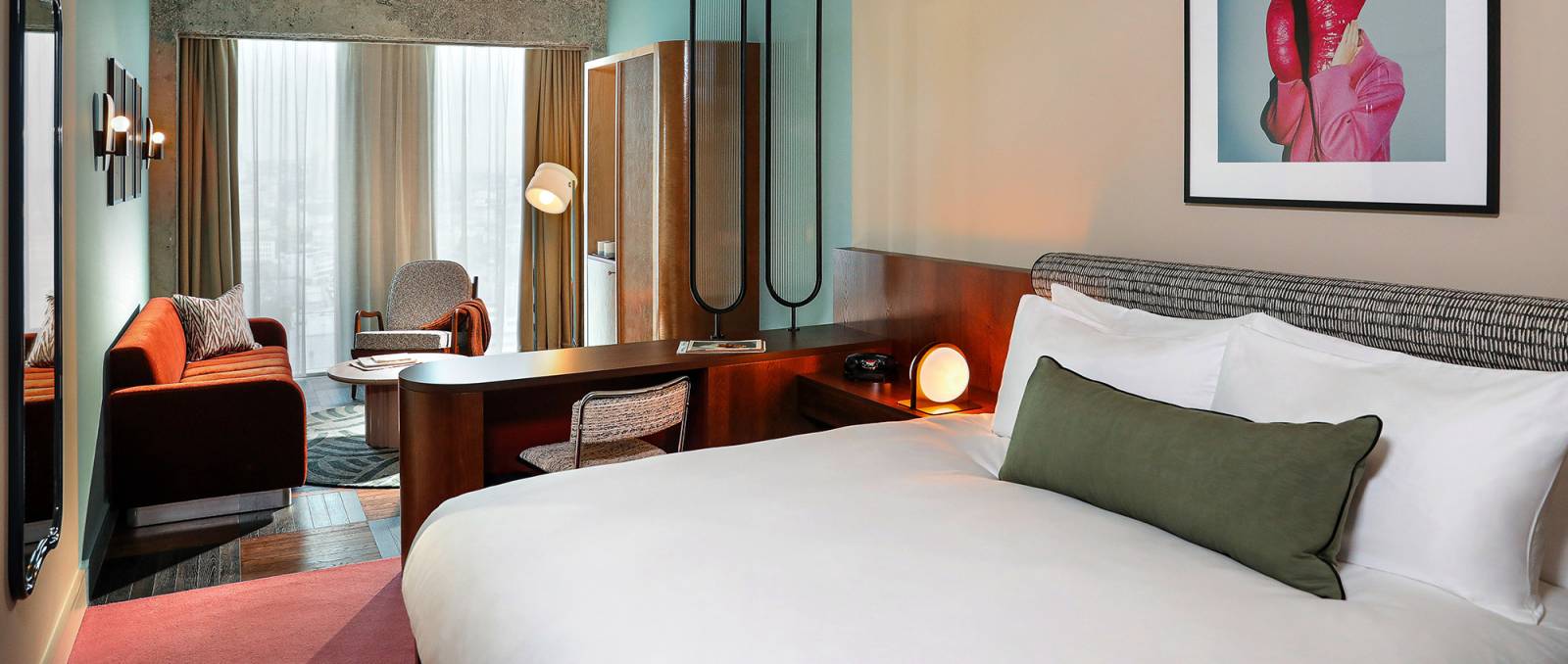 Wide view of a Biggy room with soft bed, wall art, sofa, coffee table, open wardrobe and large windows.