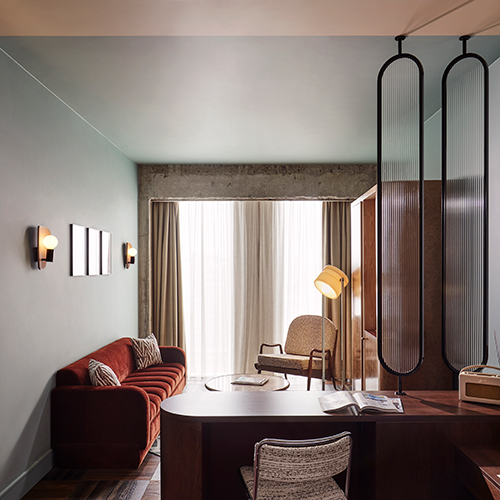 Interior shot of room at our Brussels hotel with sofa, desk, lamp and armchair by wide window.