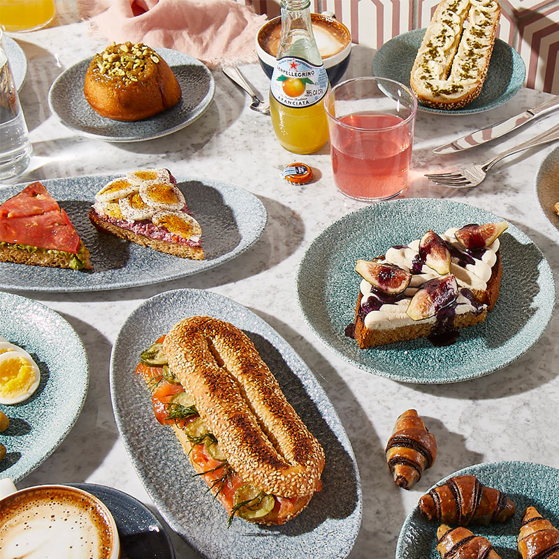 Table of food from K'far featuring sandwiches, juices and delicious desserts.