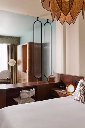 Sunlit interior of a bedroom containing comfy bed, wall art and open wardrobe.