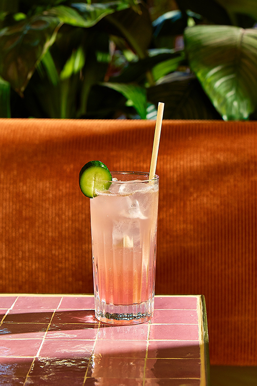 A pink cocktail with a straw and a slice of cucumber.