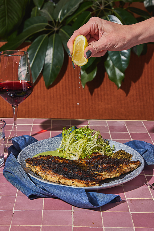 A lemon is squeezed over grilled fish.