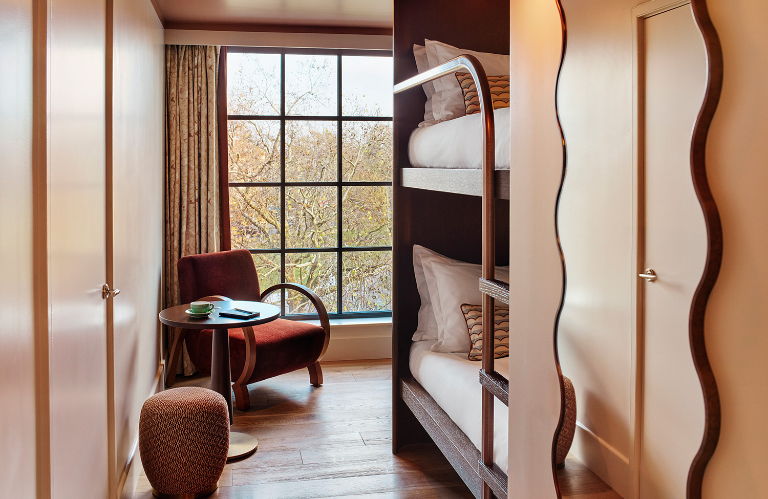 View of bunk beds, mirror and tasteful armchair with large window in room at Shepherd's Bush hotel, West London.