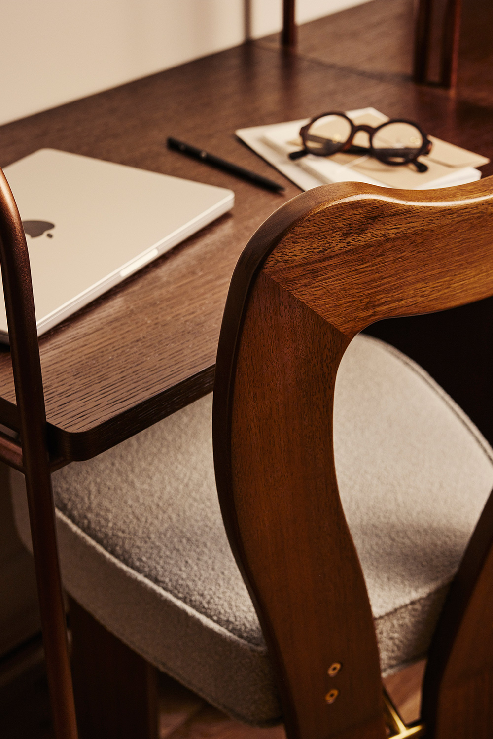 Polished wood chair with cushioned seat push under hardwood desk with papers and pens arranged on top.