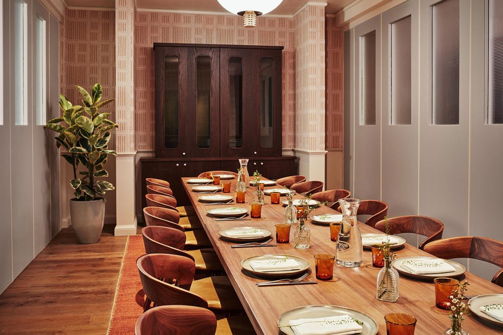 A long table is laid out in the dinning room with a large plant and a wooden cabinet in the background.