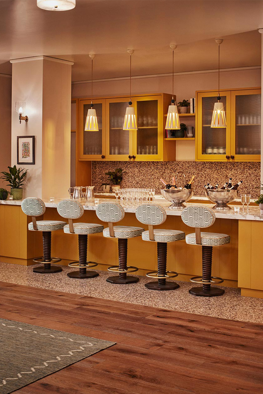 Cushioned swivel chairs sit before a brightly lit marble surface on which there are silver buckets of champagne bottles.
