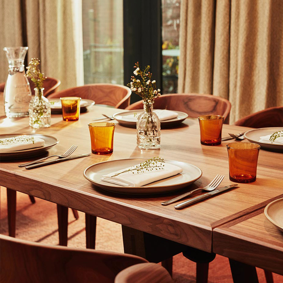 On a wooden table wait a knife and fork, plate, curved glass, napkin and a sprig of aromatic herb.
