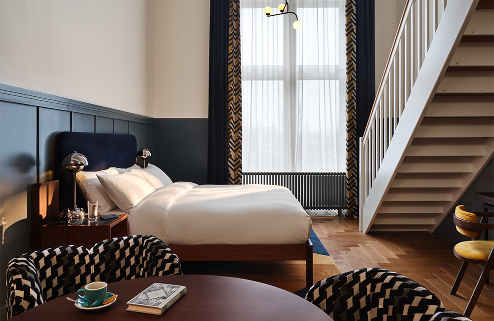 View of a large window overlooking an open-plan space with a king bed, a staircase, two chairs, and a table.