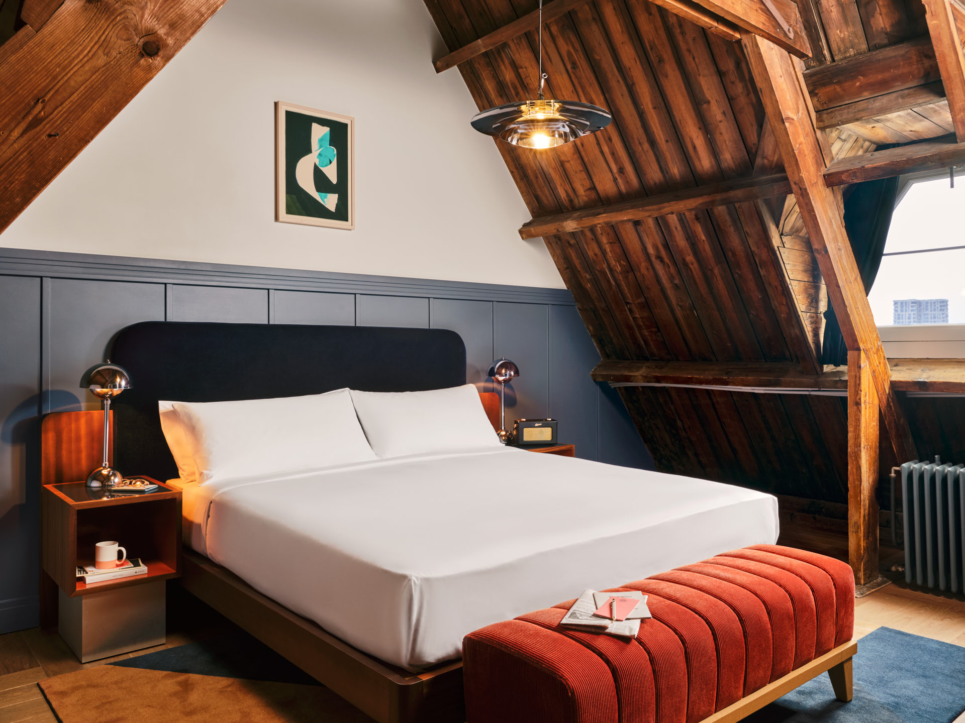 Large bed looks up to the A-frame wooden ceiling with window also seen