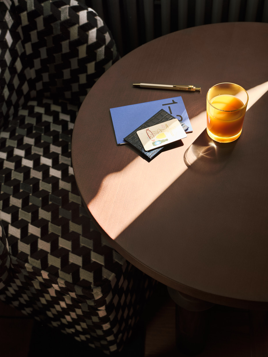 Sunlight crosses a round coffee table with a notebook and glass of fresh orange juice