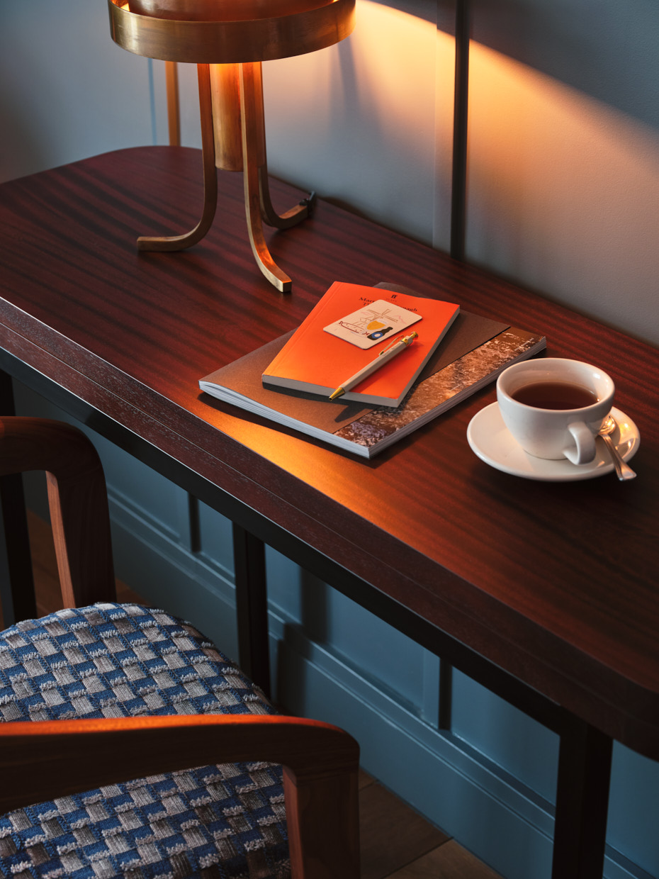 Close up of writing desk in a roo with cup of coffee and notebooks laid out under lamplight