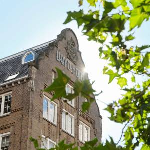 Exterior of the Lloyd hotel half hidden by sunlit leaves in the foreground