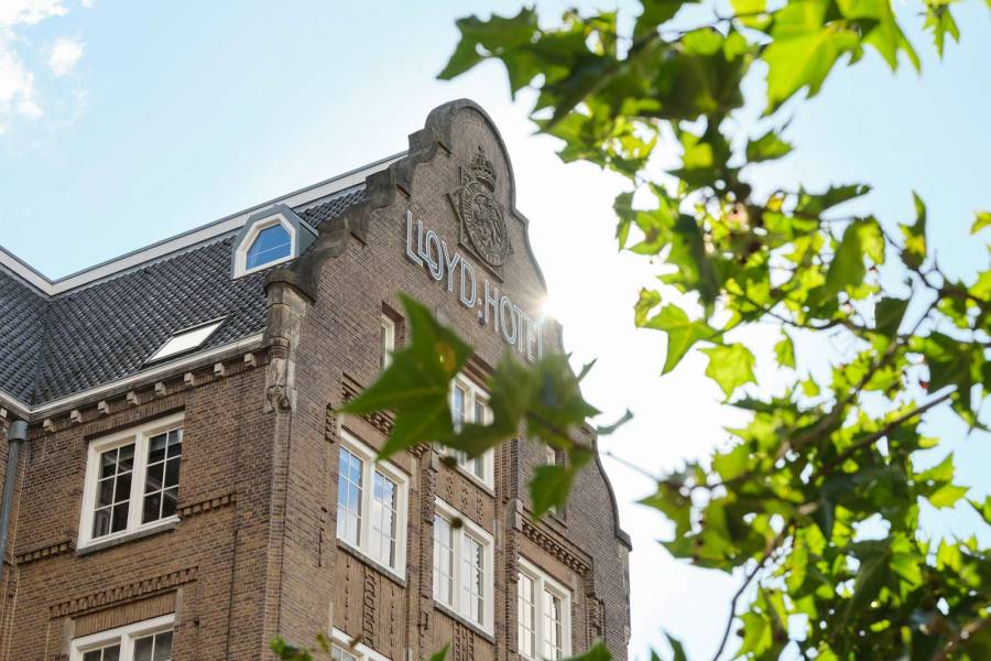 Exterior of the Lloyd hotel half hidden by sunlit leaves in the foreground