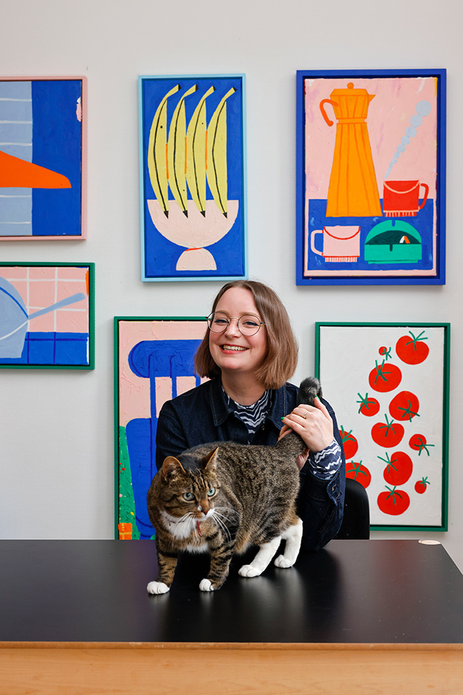 Dutch artist Frederique Matti sits with her cat before a wall of her paintings.