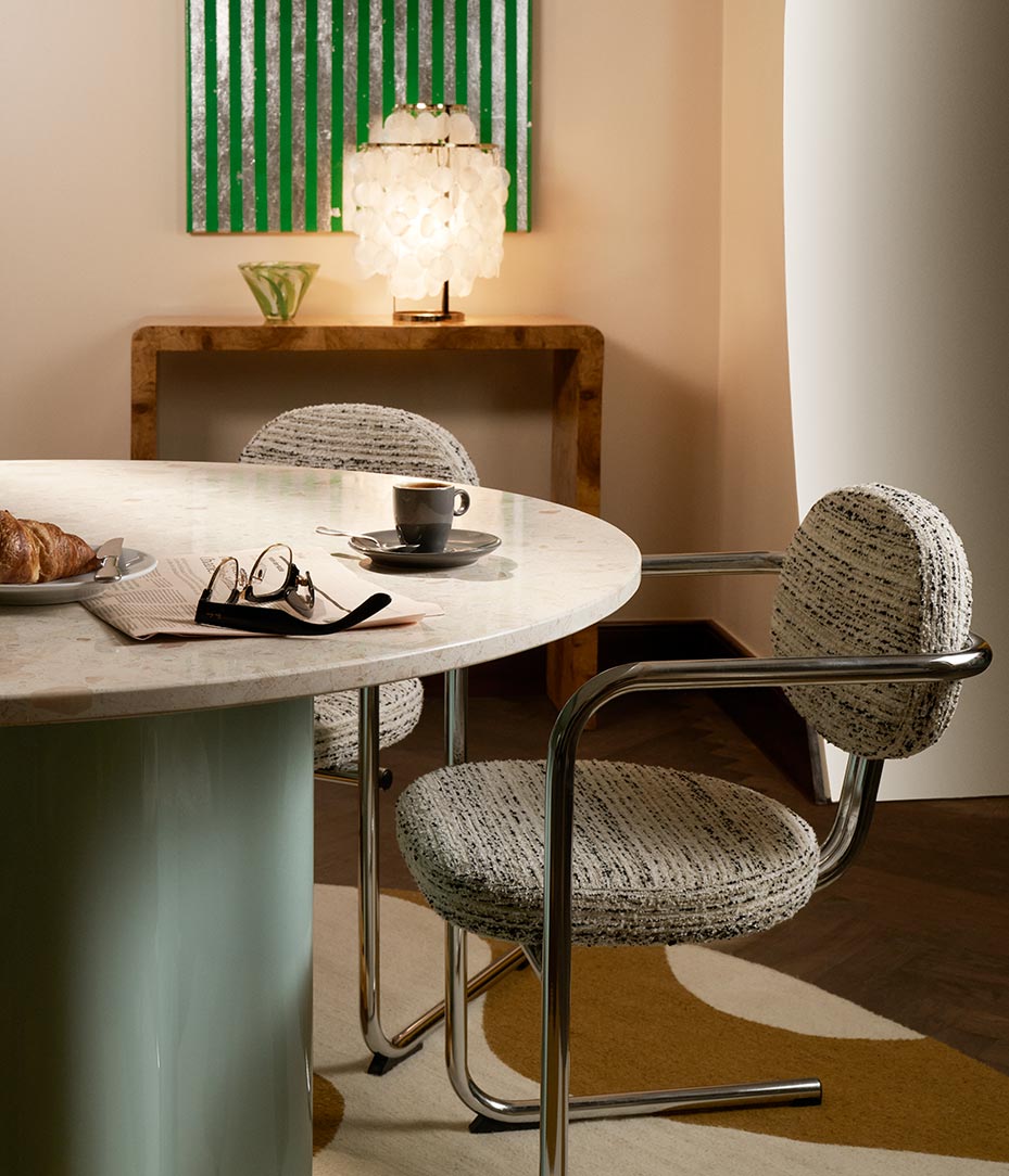 Close up of table and chair with table lamp in rear and coffee and spectacles resting on the marble tabletop.
