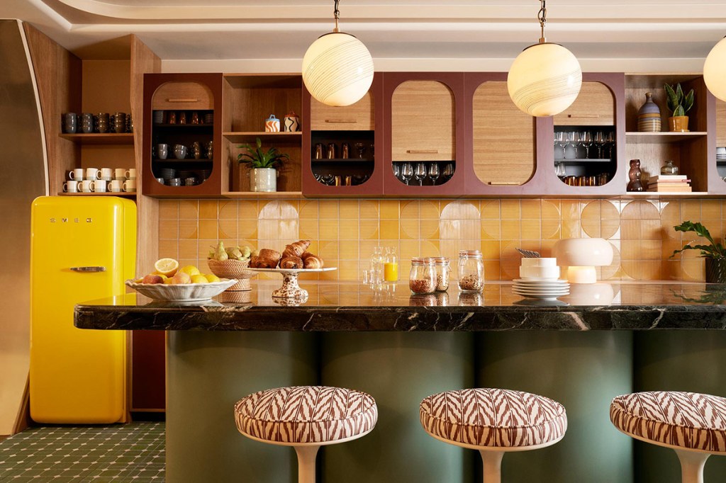 Pamtry interior with fresh fruit and pastries on a marble kitchen island ringed with stools.