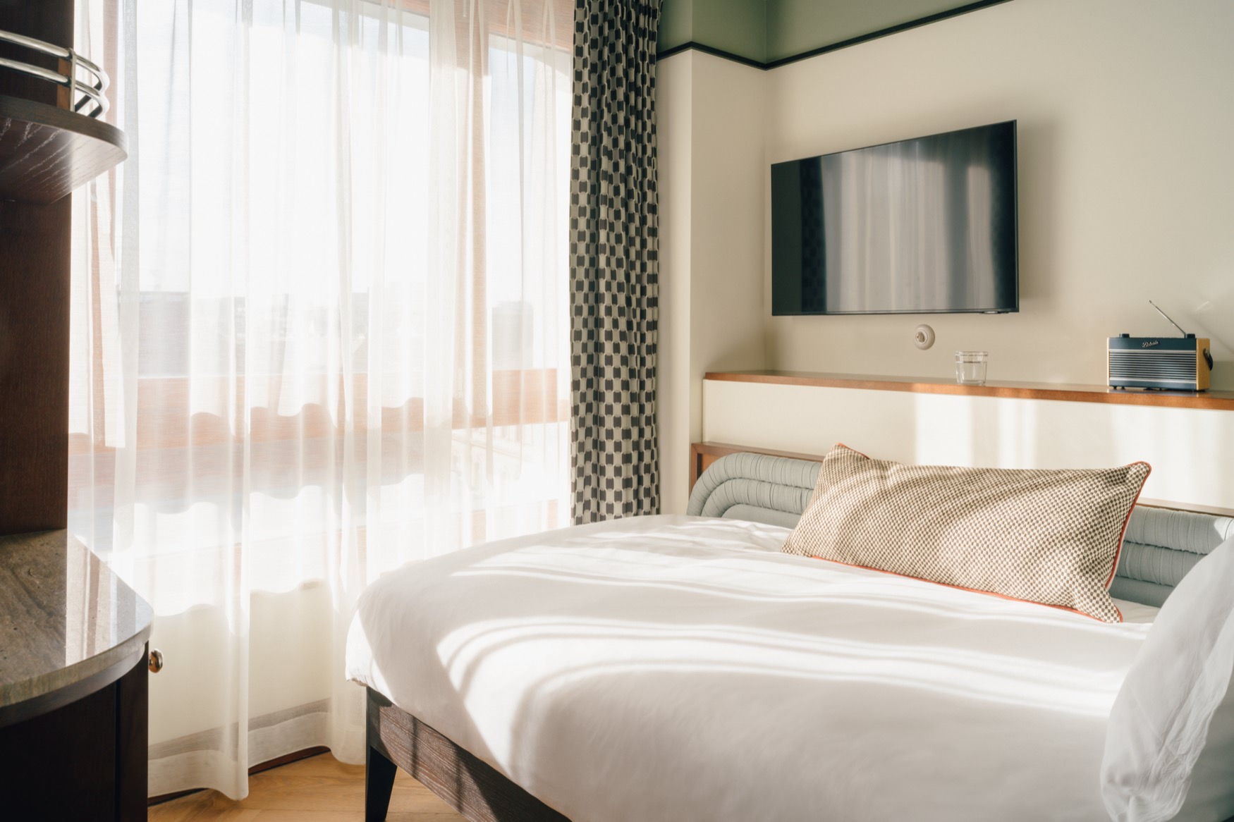 Single bed in corner with large window at the end of bed.