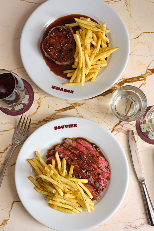 two plates with steak and chips with a glass of water and red wine.