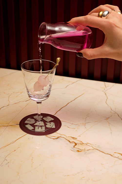 Hand pouring a bright purple cocktail liquid into a glass.