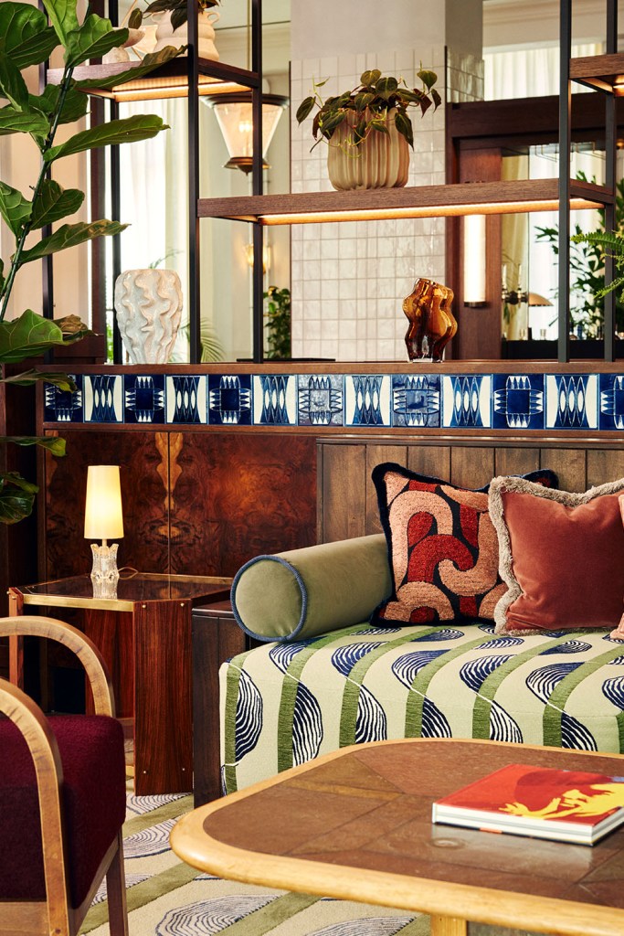 Green velvet sofa with cousion infront of a bookcase and coffee table and chair infront of it.