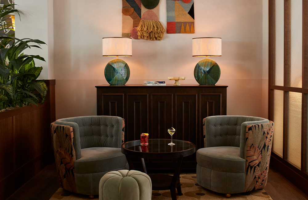 two arm chairs in a corner with console table and table lamps.