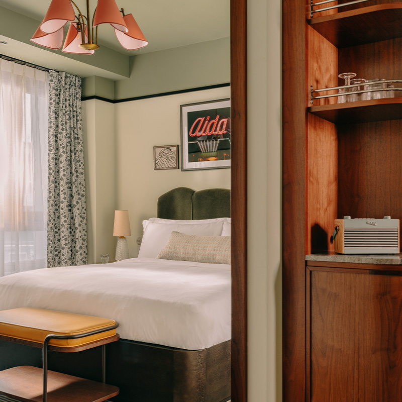 A view into one of the rooms in Vienna, showcasing a large bed, open display wardrobe and large window.