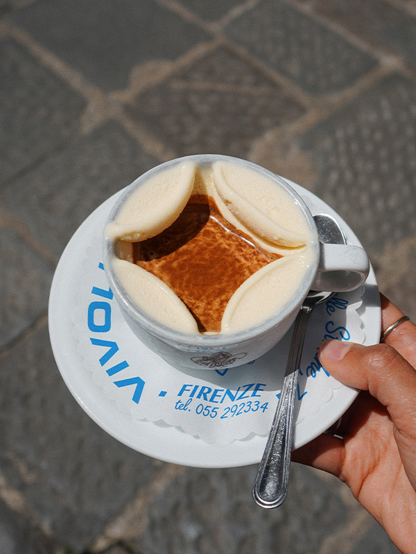 A hand holding a cup of coffee with frothy foam decorated in the shape of a diamond
