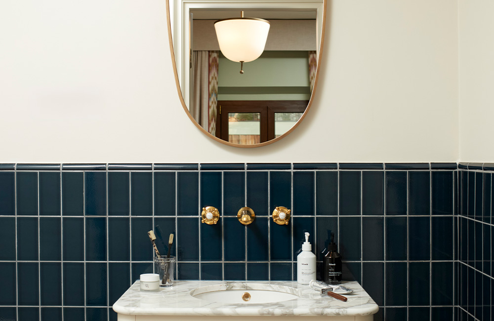 Blue and white tiled bathroom featuring a gold-rimmed mirror, a porcelain sink, and brass water knobs