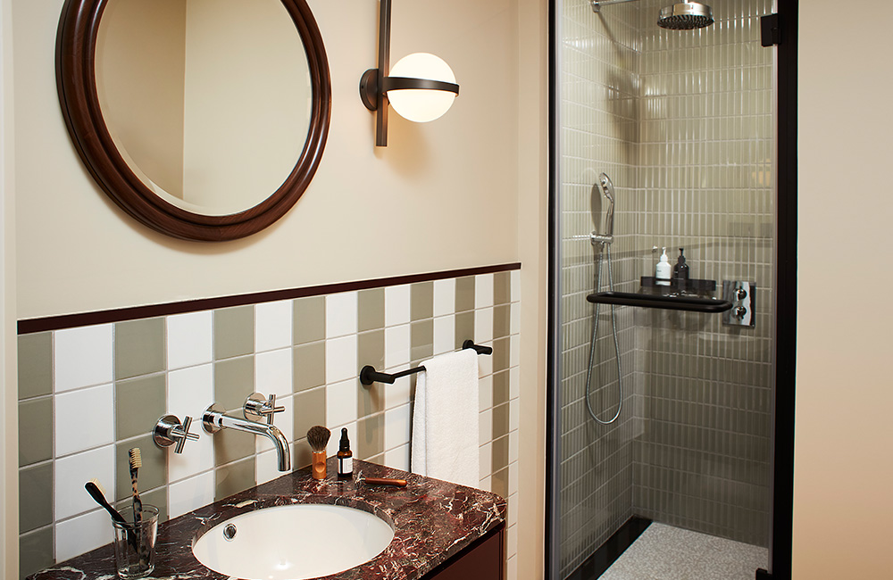 Bathroom sink with a large wooden-framed mirror and a basin in stunning brown marble, a walkin' rainshower, set against white and green tiled walls.