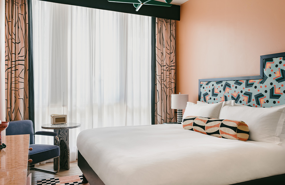 Side view of a coral-coloured cozy terrace with natural light illuminating a king-size bed, an armchair, and a side table in a corner.