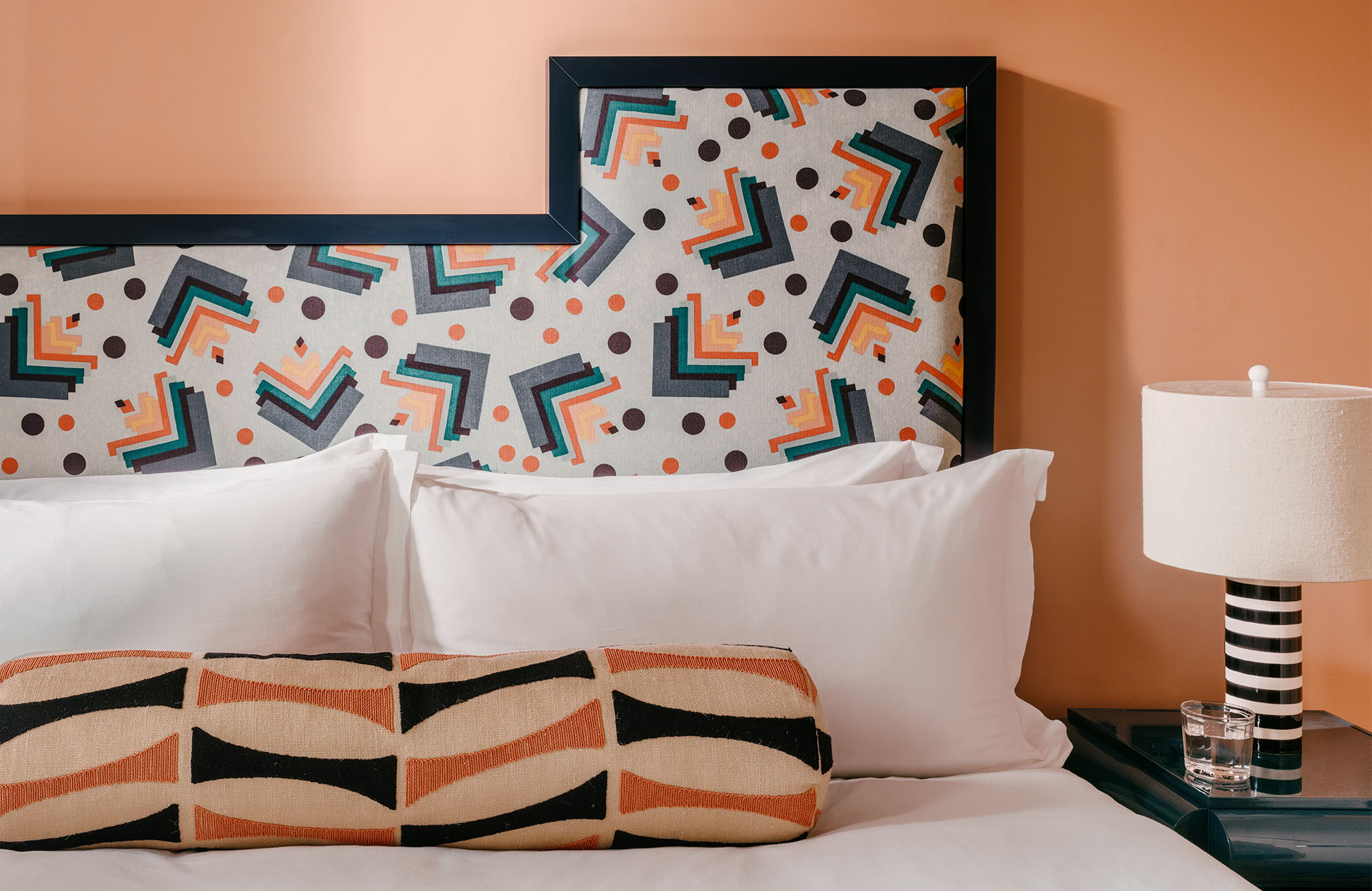 Headboard with a bright, dynamic pattern, large fluffy pillows, and a black and white lamp beside it.
