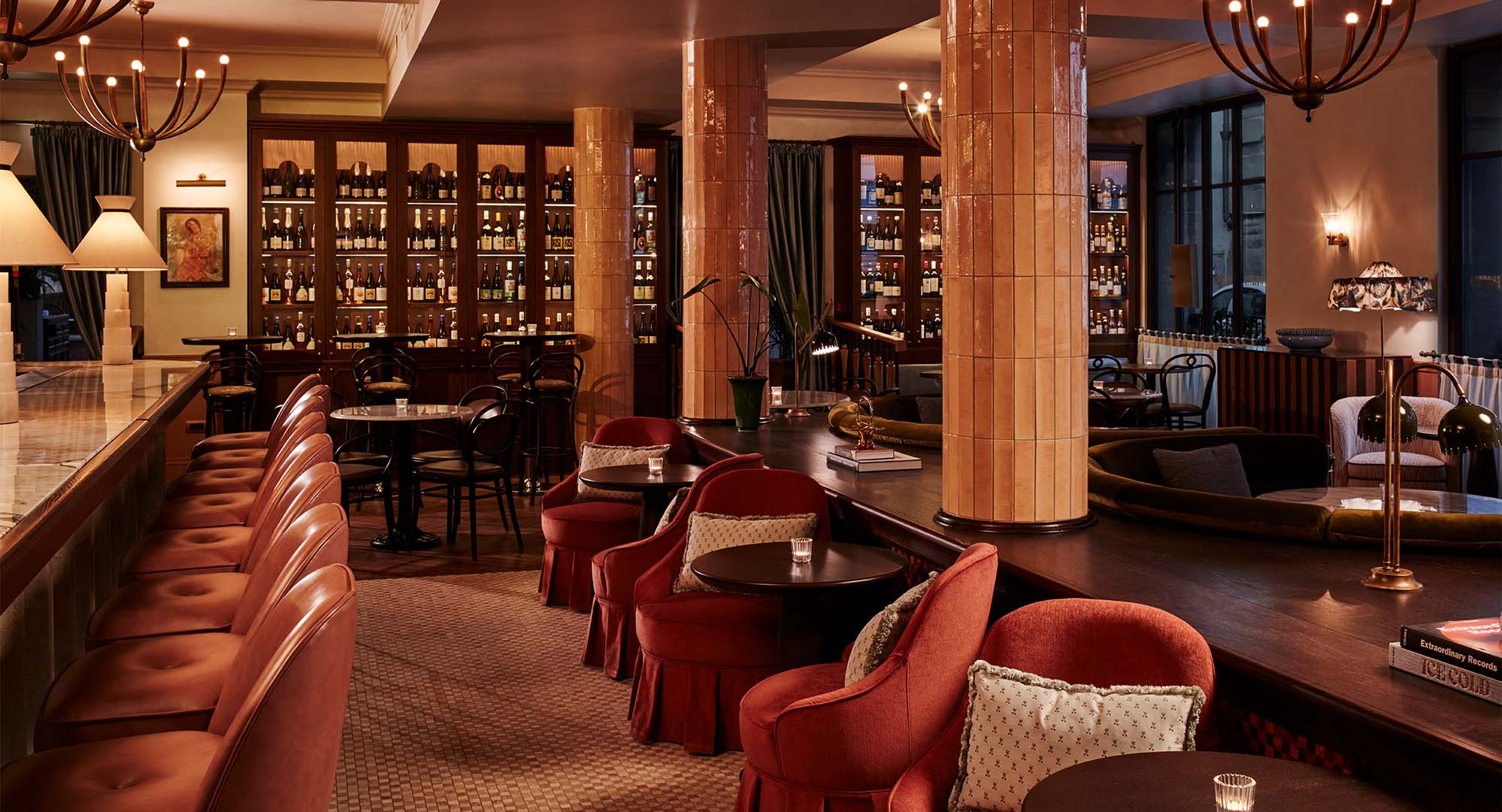 Interior of Enoteca Violetta, which features a long marble bar with comfy red velvet bar stool, and clusters of armchairs with tables.