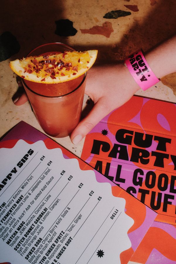 hand resting a drink on a table with the gut party menu on display.
